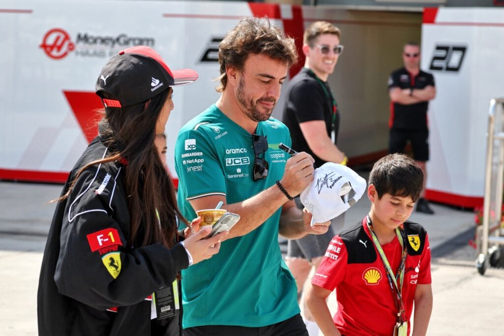 Fans get a cap signed by Fernando Alonso during a paddock tour